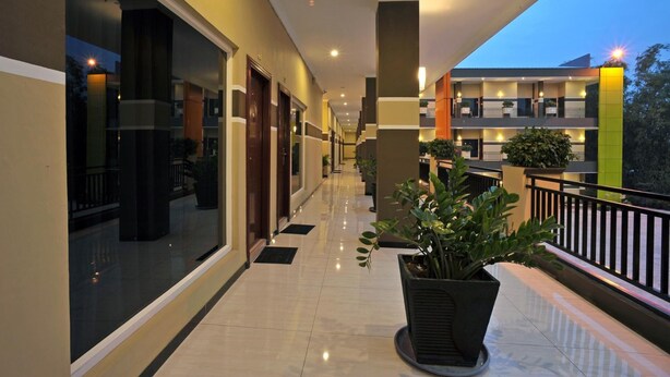 A hotel corridor with a reflective floor, large windows, and potted plants. - Hotel New Merdeka Pati (Pati)
