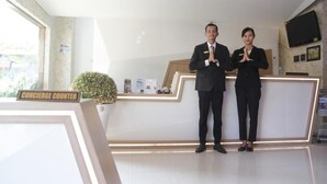 A reception desk with a concierge counter, a potted plant, and a television mounted on the wall. - Hotel New Merdeka Pati (Pati)