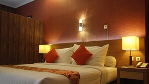 A hotel room with a bed, two bedside lamps, a nightstand with a phone, and a wooden headboard. - Hotel New Merdeka Pati (Pati)