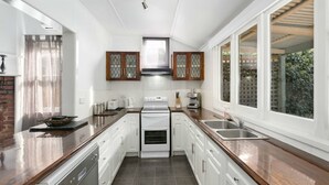 A modern kitchen with white cabinetry, a central island, and a large window providing natural light. - Magnolia cottage Healesville (Healesville)