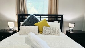 A neatly made bed with white bedding, a rolled white towel, and decorative pillows in various textures and colors. - Magnolia cottage Healesville (Healesville)