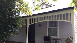 A covered porch with a wooden deck, a table, two chairs, and a window with a curtain. - Magnolia cottage Healesville (Healesville)