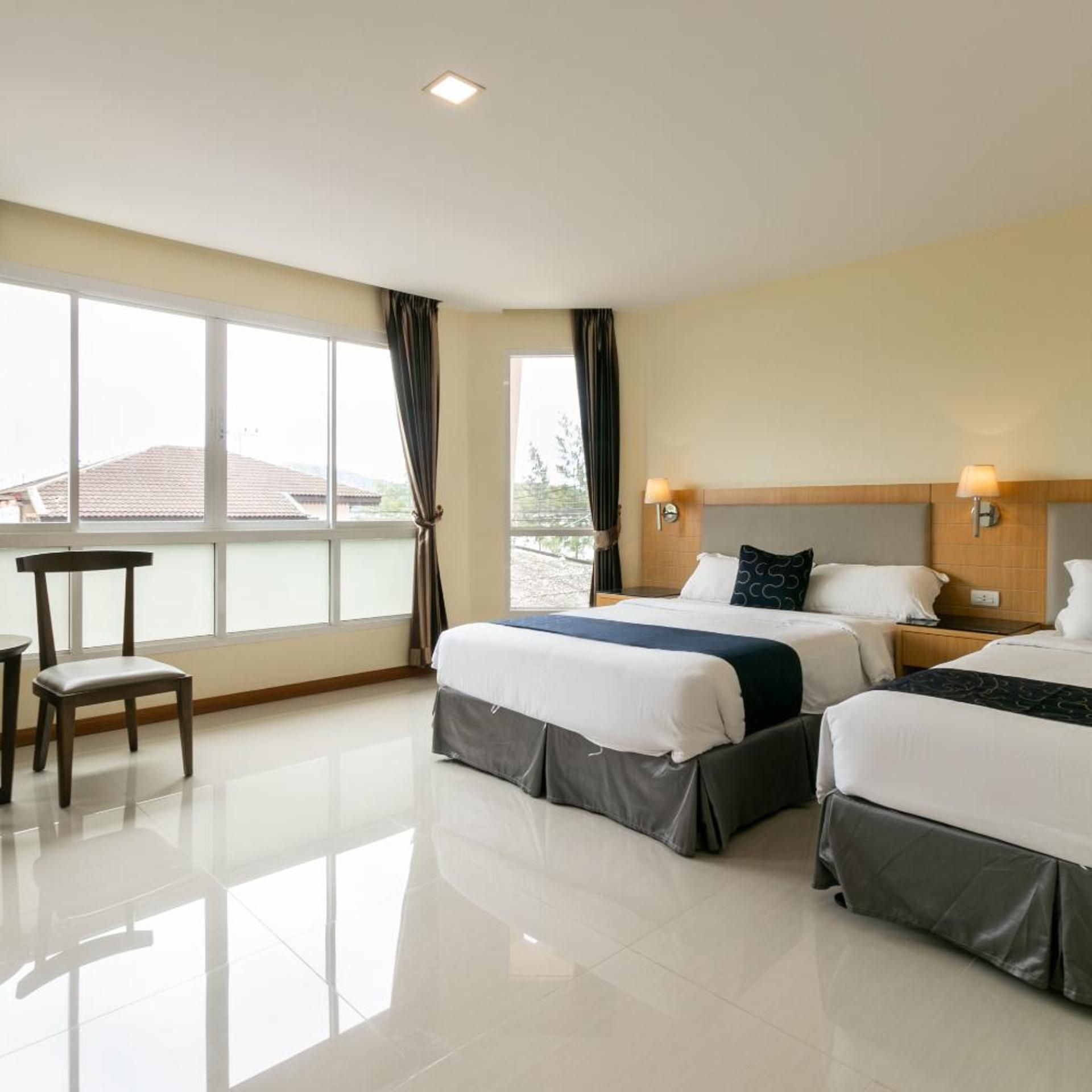 A hotel room with two beds, a chair, a table, and a large window.