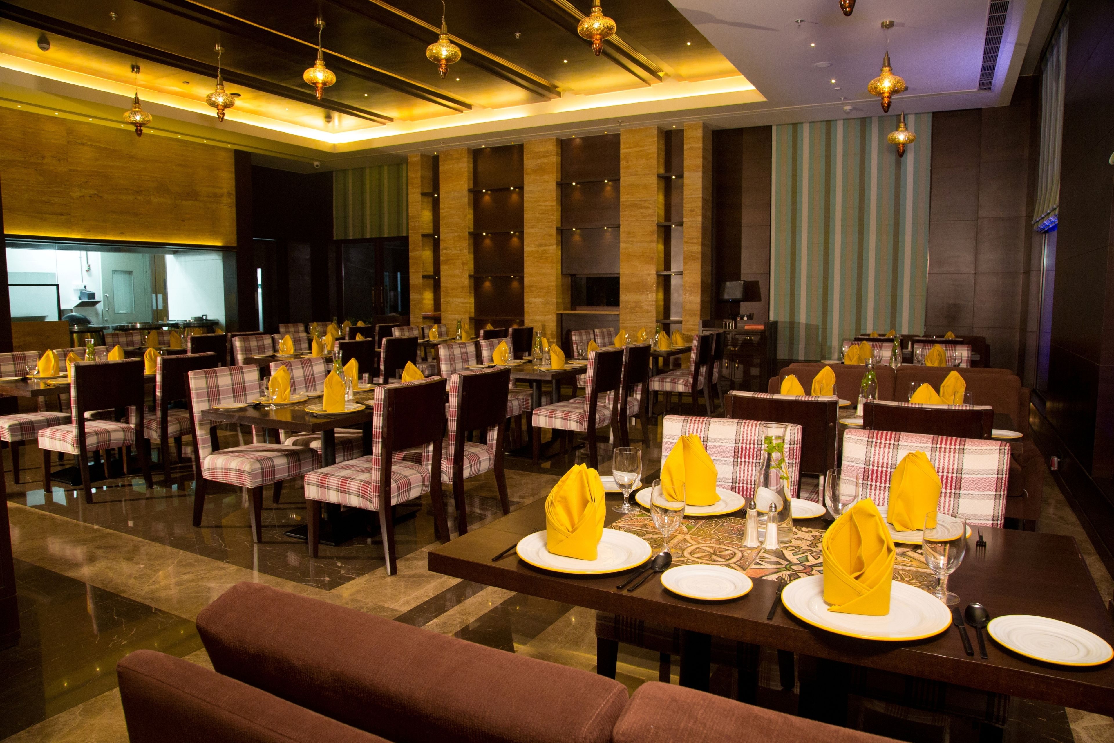 A restaurant with multiple dining tables set with yellow napkins, white plates, and cutlery.