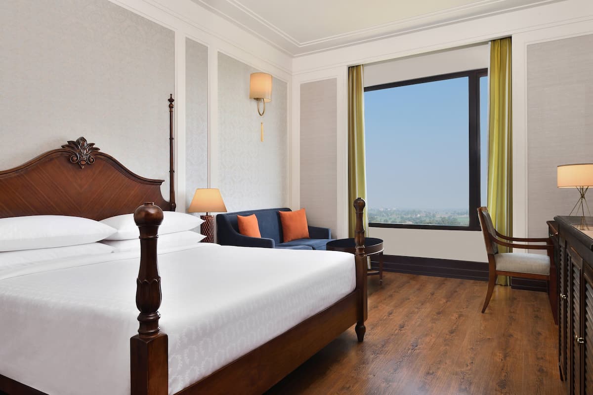 A hotel room with a large bed, a sofa, a desk, and a view of the city.