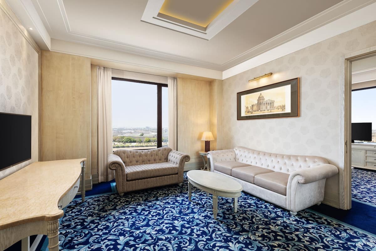 A hotel room with a large window, a sofa, a small table, and a TV.