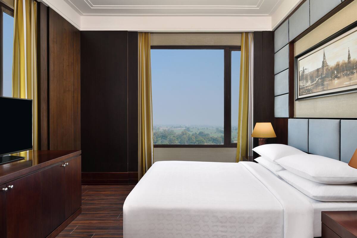 A hotel room with a large bed, a television, a nightstand, and a window with a view of the city.