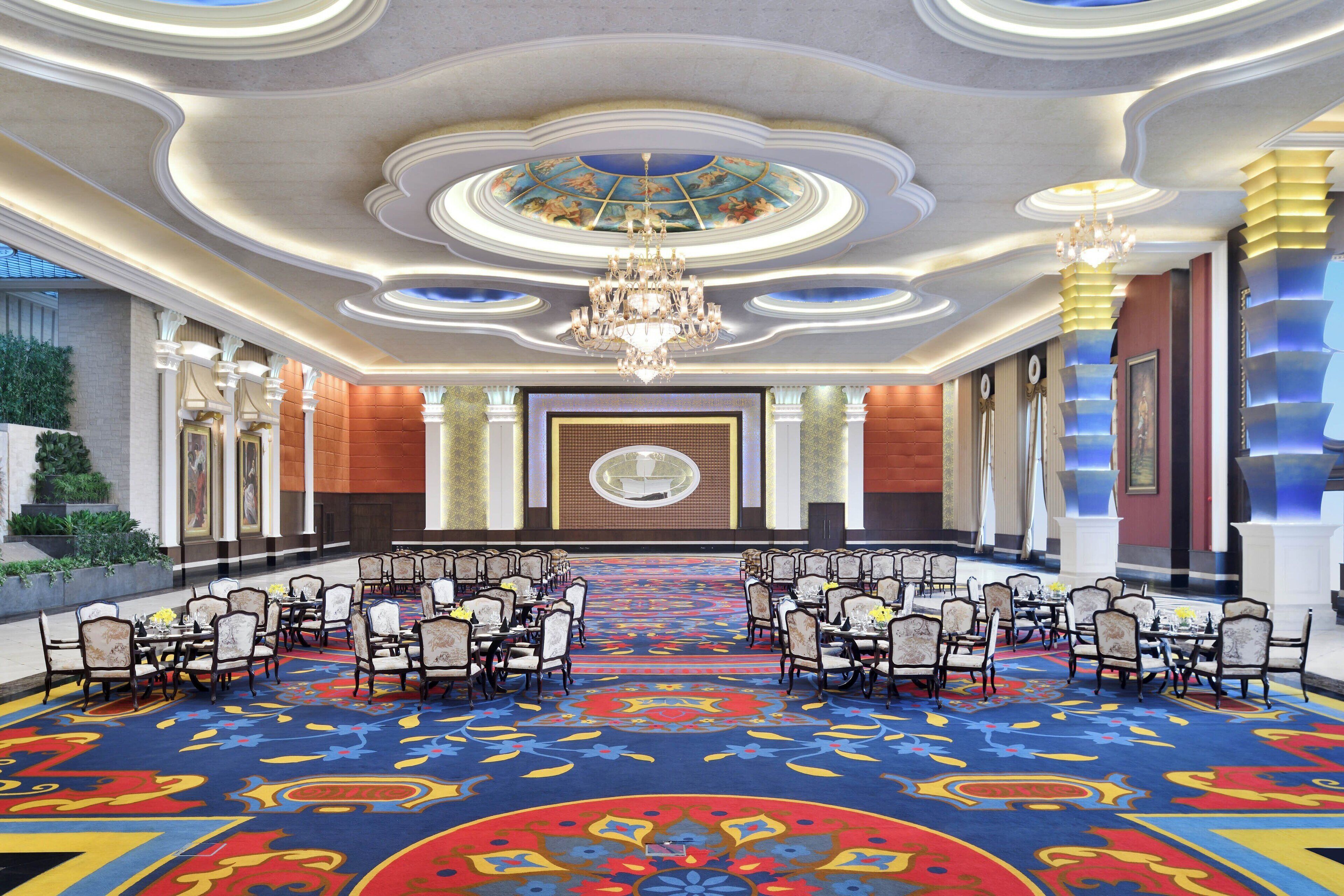 A spacious conference room with a patterned carpet, rows of chairs, and a chandelier.
