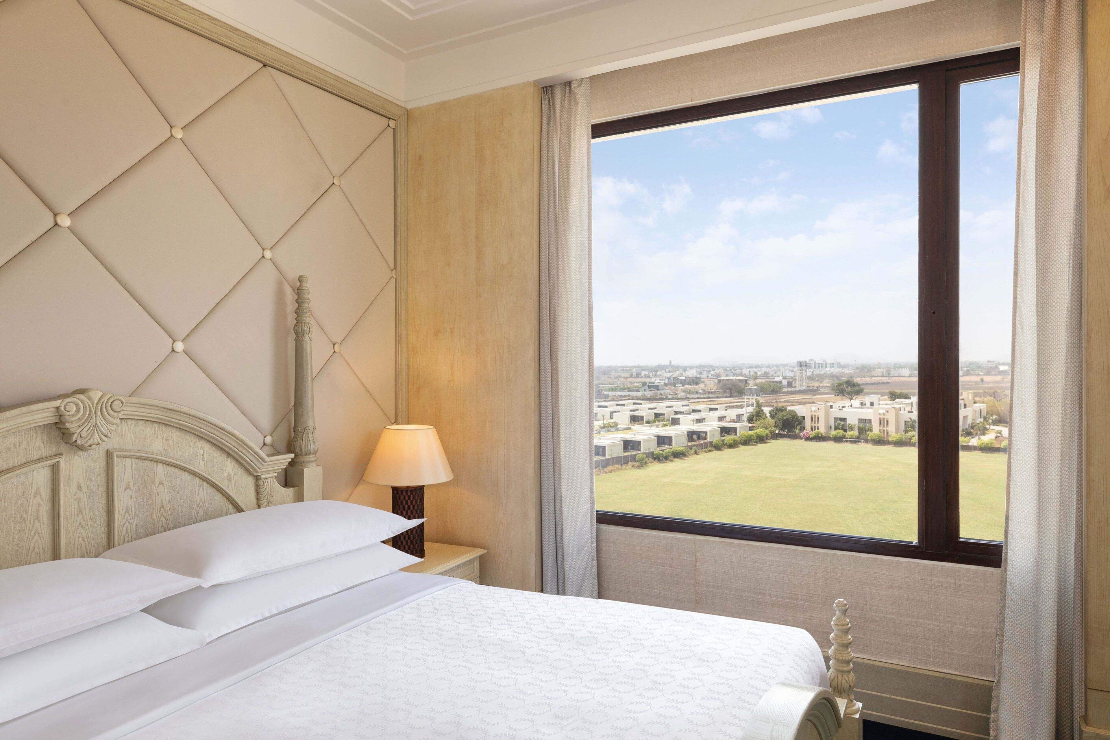 Una habitación de hotel con una cama grande, una mesita de noche, una lámpara y una ventana con vistas a la ciudad.