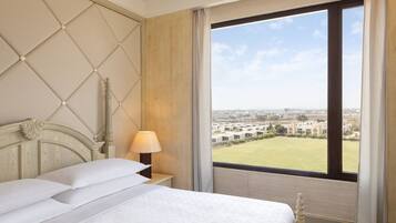 Una habitación de hotel con una cama grande, una mesita de noche, una lámpara y una ventana con vistas a la ciudad.