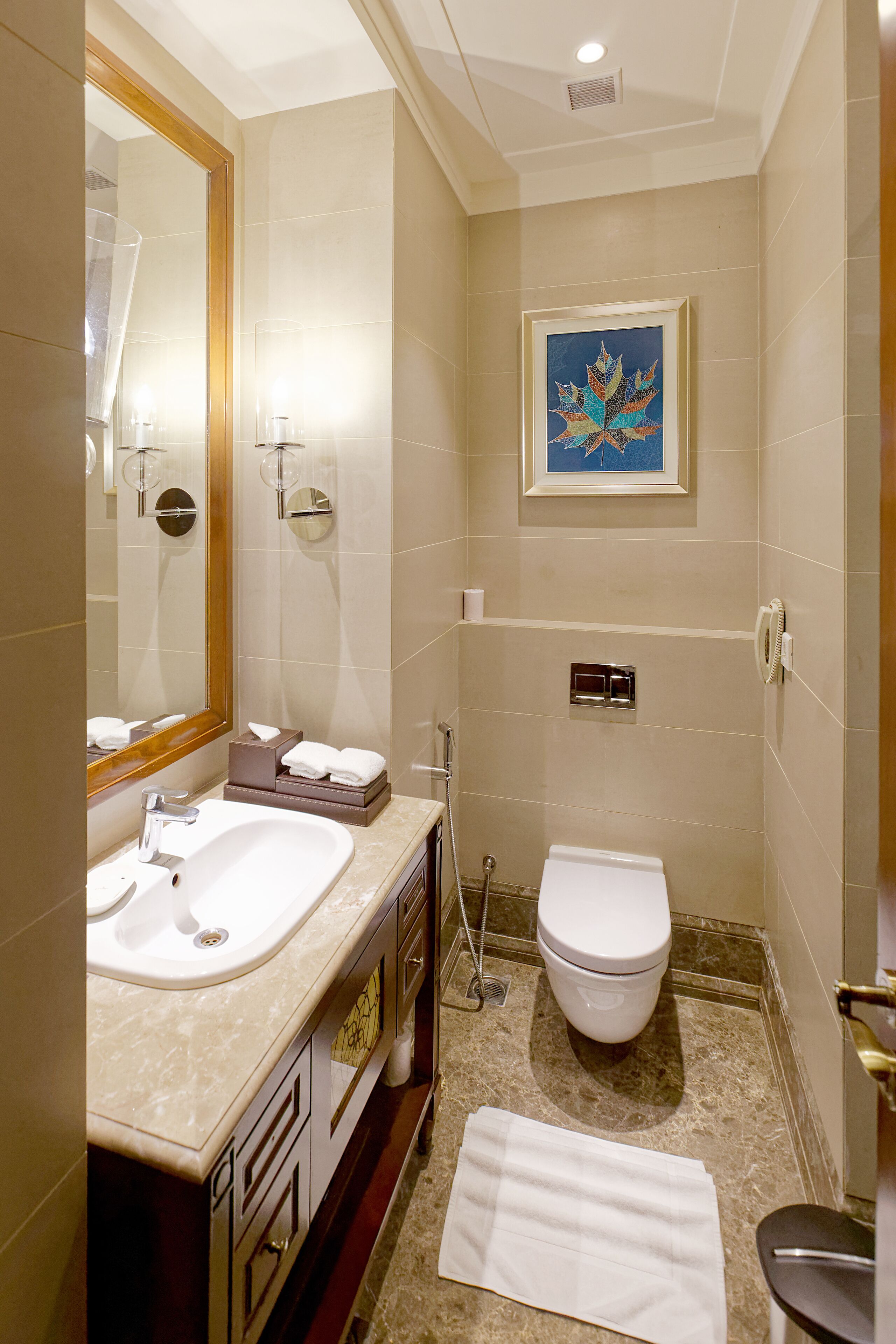 A bathroom with a sink, mirror, toilet, and a framed artwork on the wall.