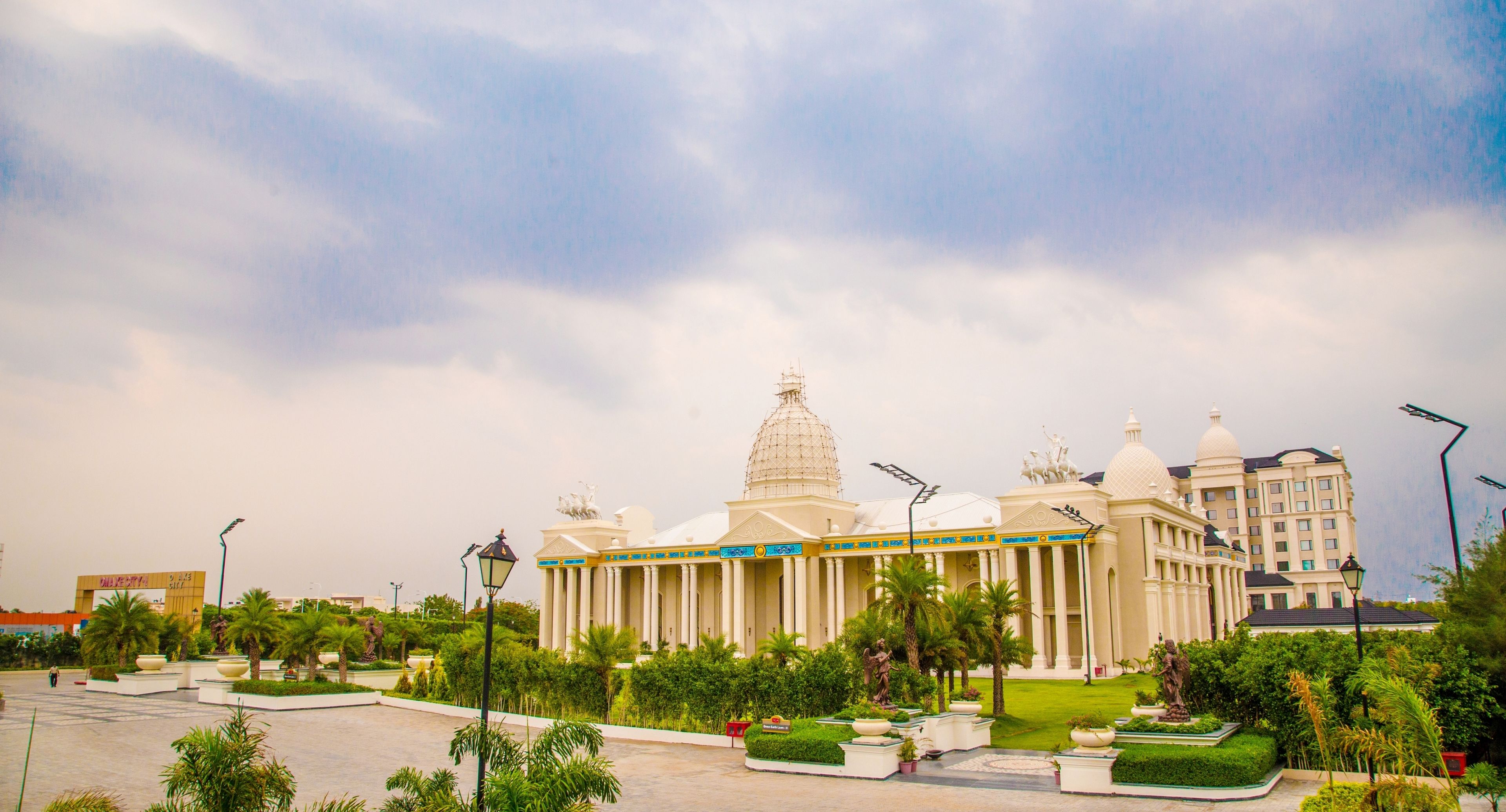 A large, white building with a central dome and columns, surrounded by palm trees and greenery.
