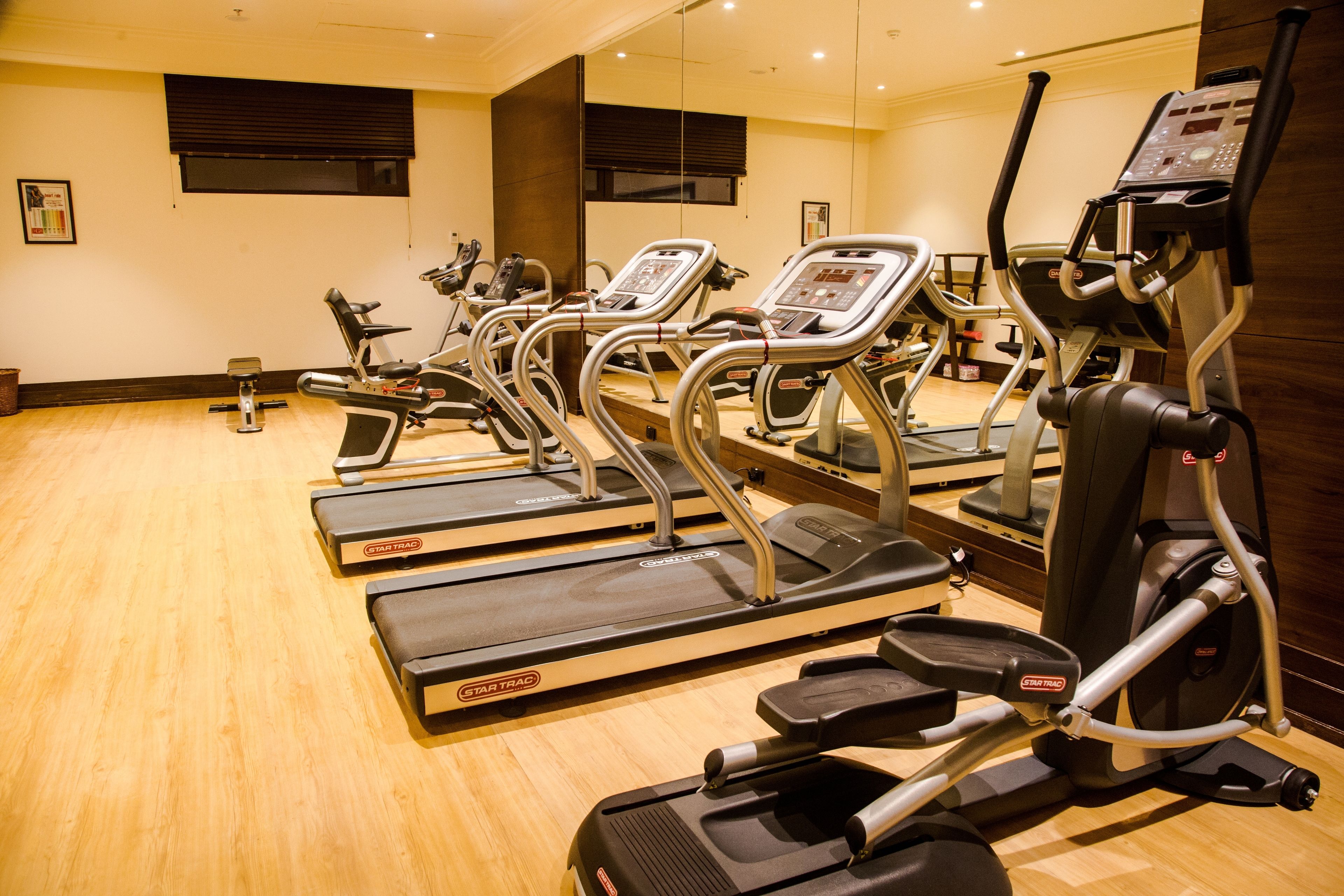 A gym with multiple treadmills and exercise bikes, wooden flooring, and mirrors on the walls.