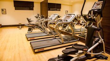 A gym with multiple treadmills and exercise bikes, wooden flooring, and mirrors on the walls.