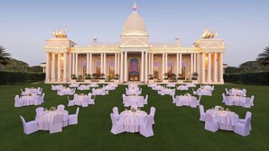 A large, elegant building with a central dome and symmetrical wings, surrounded by a formal outdoor seating area with round tables and white chairs. - Sheraton Grand Palace Indore (Indore)