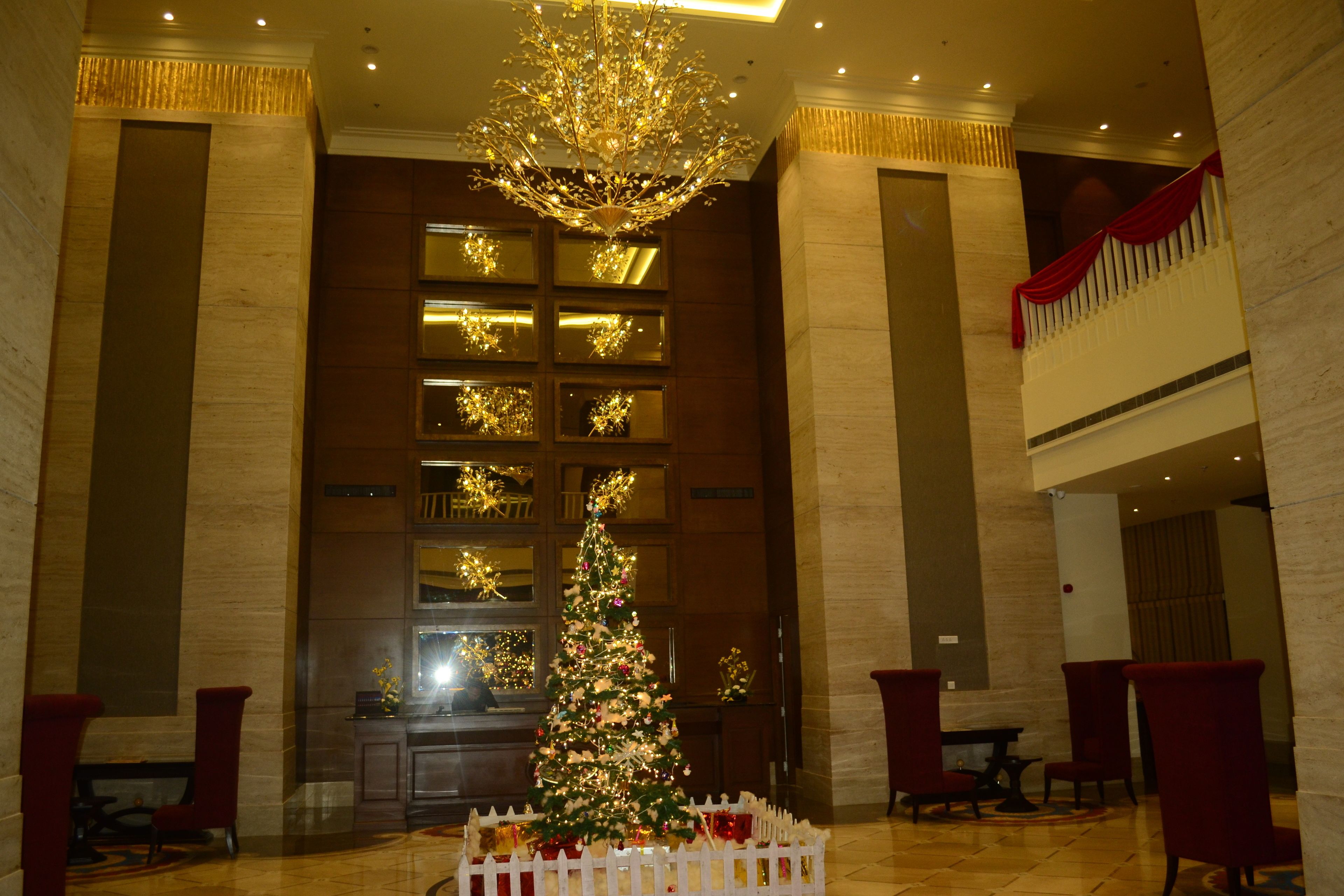 A lobby with a large Christmas tree, a chandelier, and red chairs.