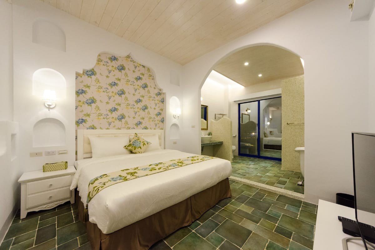 A bedroom with a bed, nightstand, and a bathroom with a shower and sink.