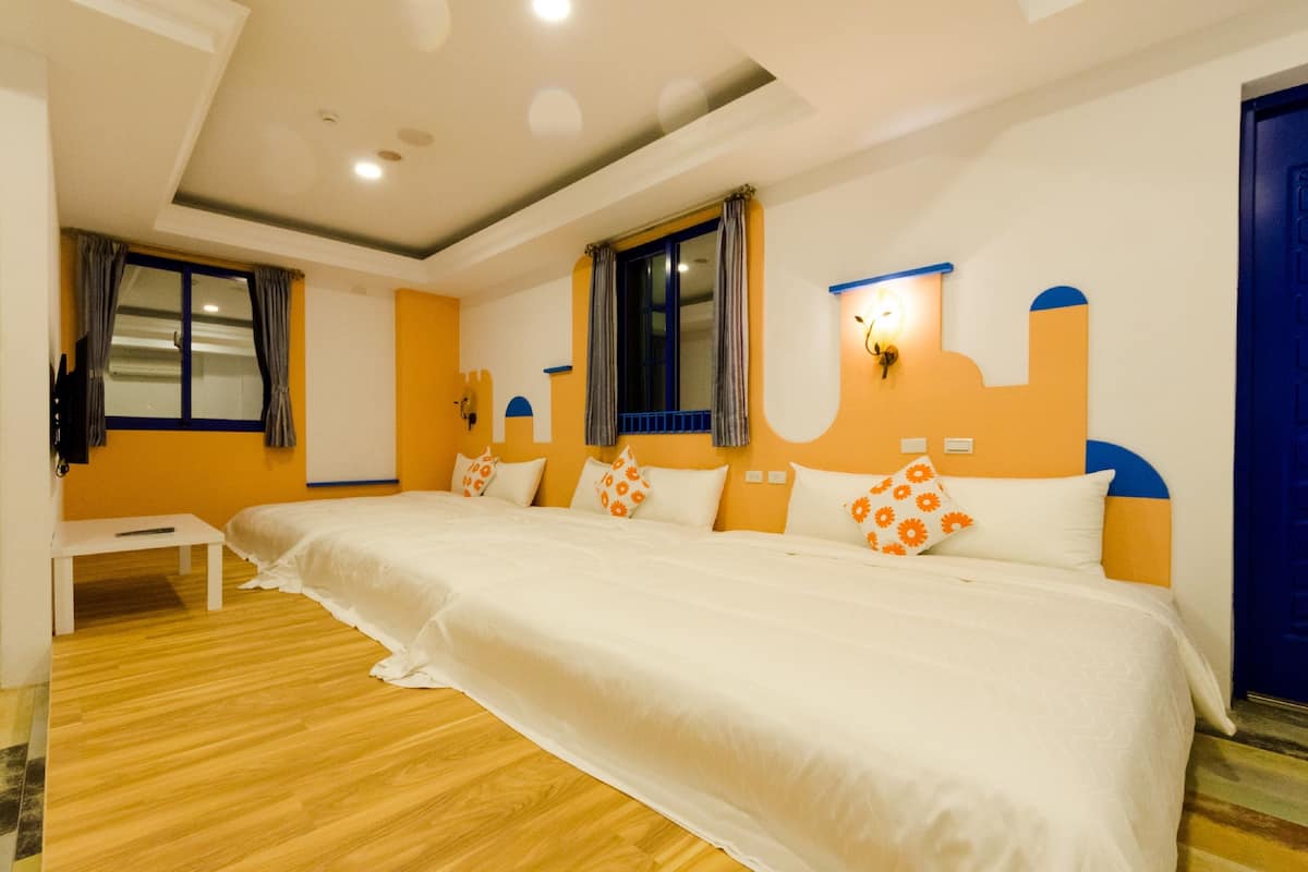 A hotel room with a large bed, a small table, and two windows with curtains.