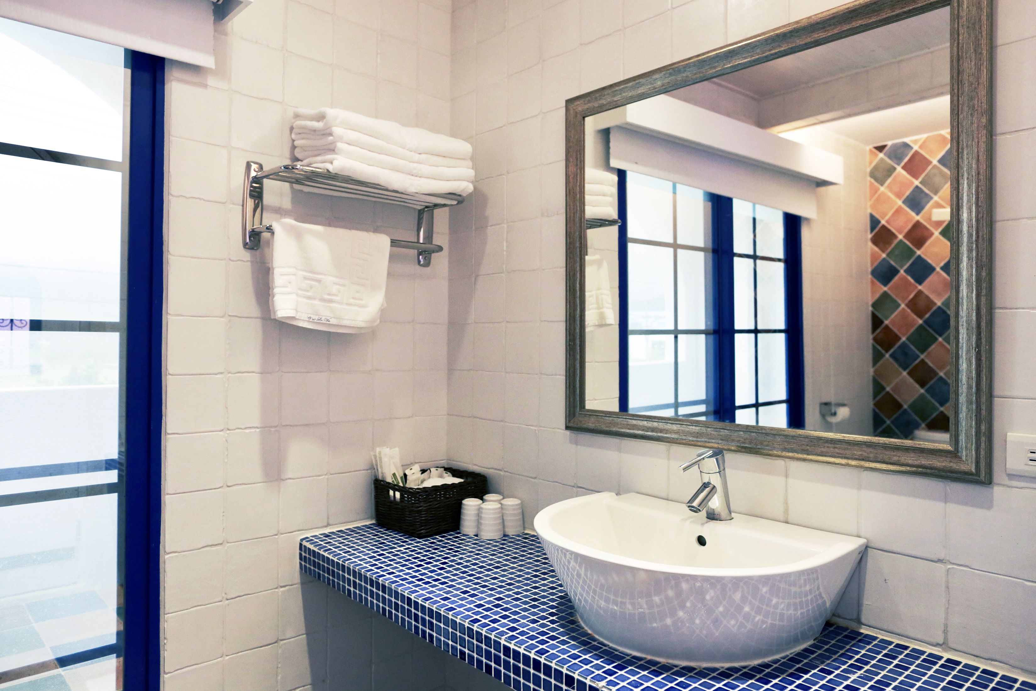 Un baño con lavamanos blanco, encimera con azulejos azules, un espejo y un perchero con toallas dobladas.