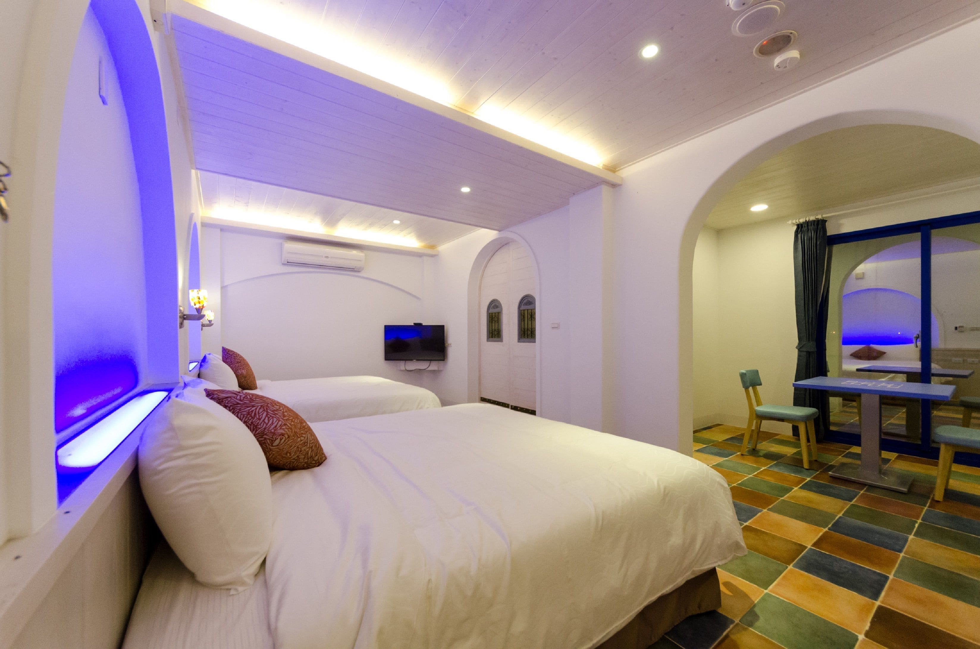 Una habitación de hotel con dos camas, televisión y zona de comedor con sillas y mesa.