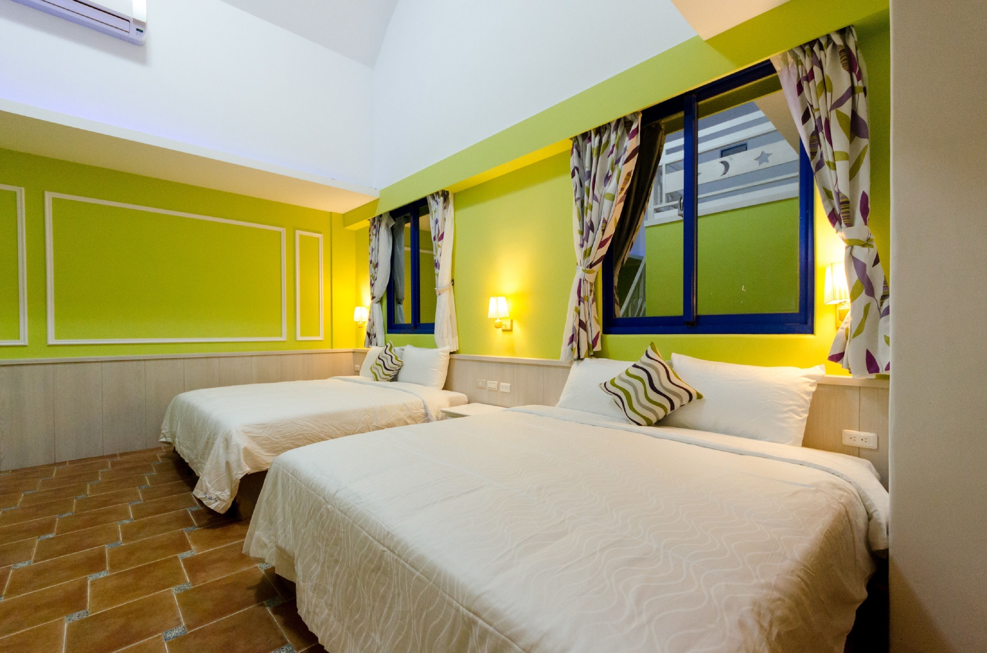 A hotel room with two beds, a tiled floor, and a window with curtains.