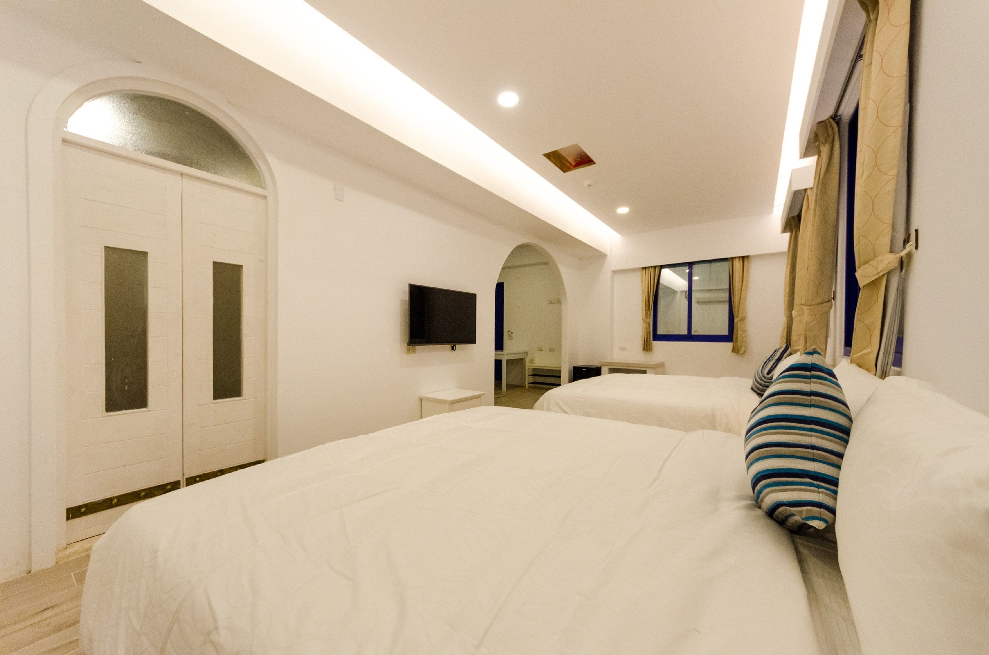 A hotel room with two beds, a TV, a desk, and a bathroom.