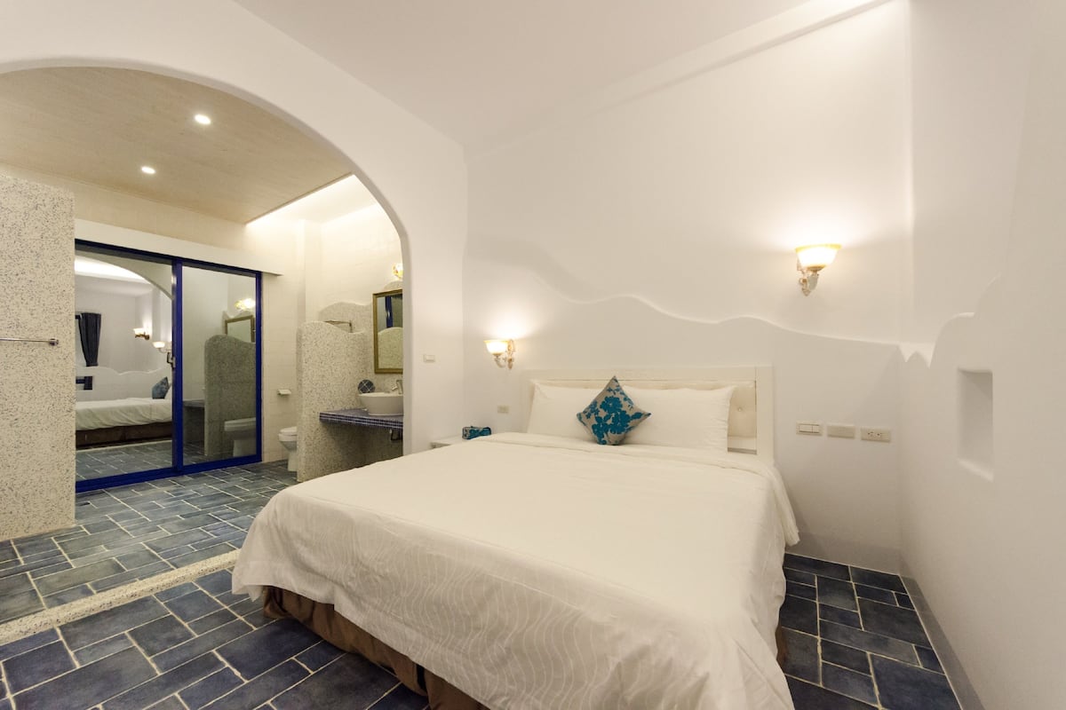 A hotel room with a large bed, a bathroom with a shower, and a view of the outside.