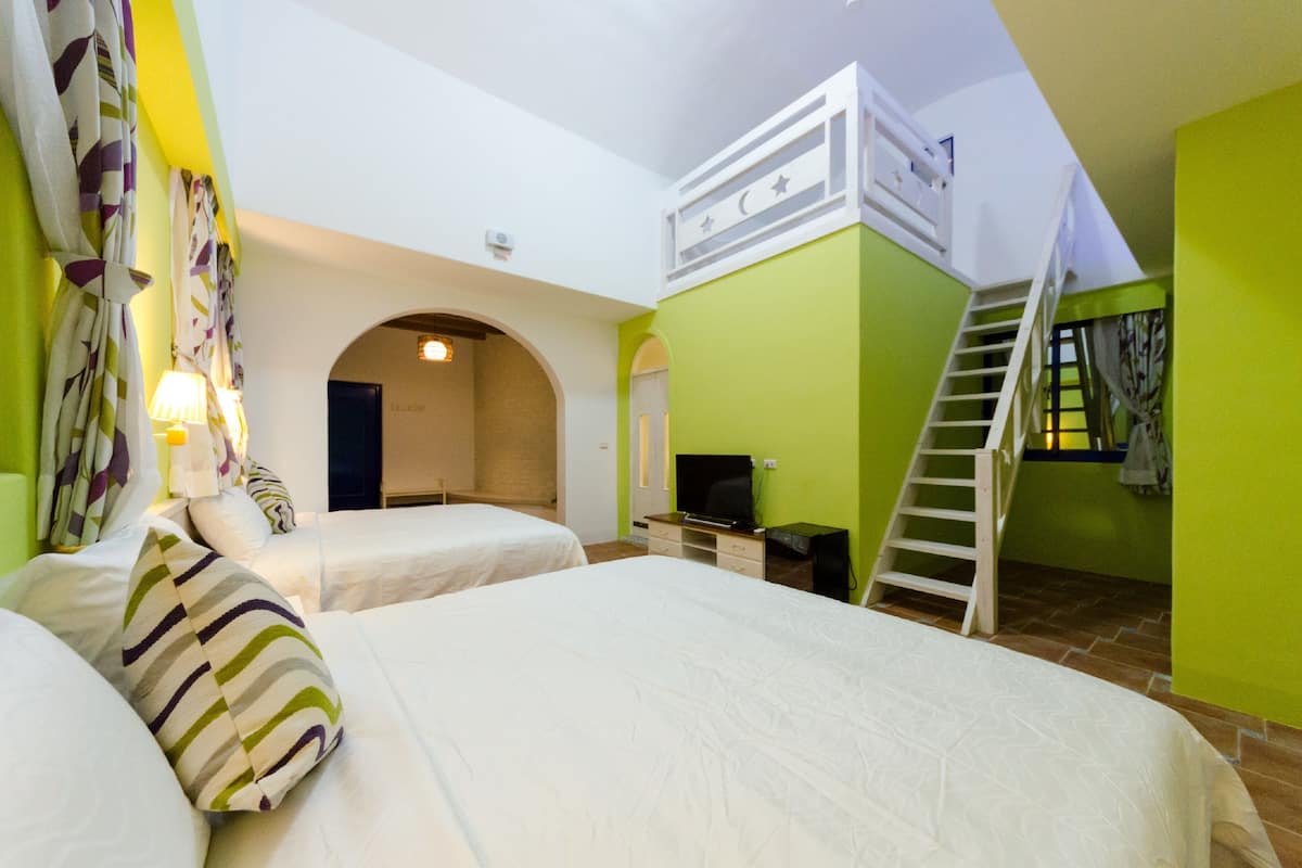 A room with two beds, a TV, a desk, and a staircase.
