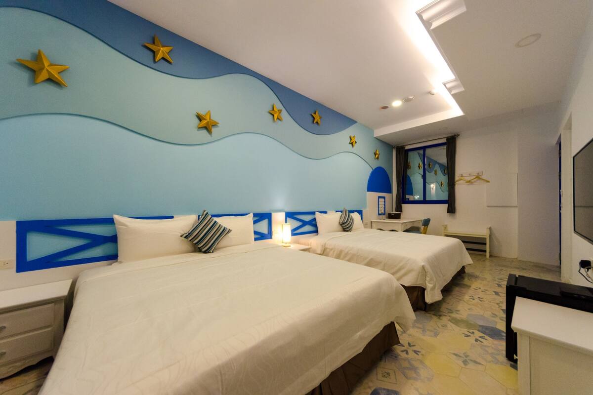A hotel room with two beds, a TV, and a desk.