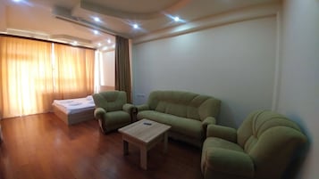 Een woonkamer met een bank, twee fauteuils, een houten salontafel en een bed met een witte matras.