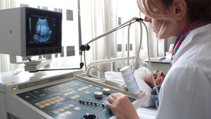 A medical ultrasound machine with a monitor displaying an ultrasound image, a control panel, and a patient lying on a bed. - Cross Health Center (Yerevan)