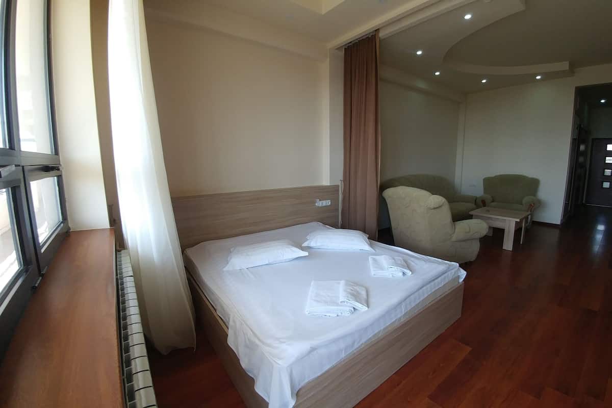A hotel room with a large bed, a chair, a small table, and a door.