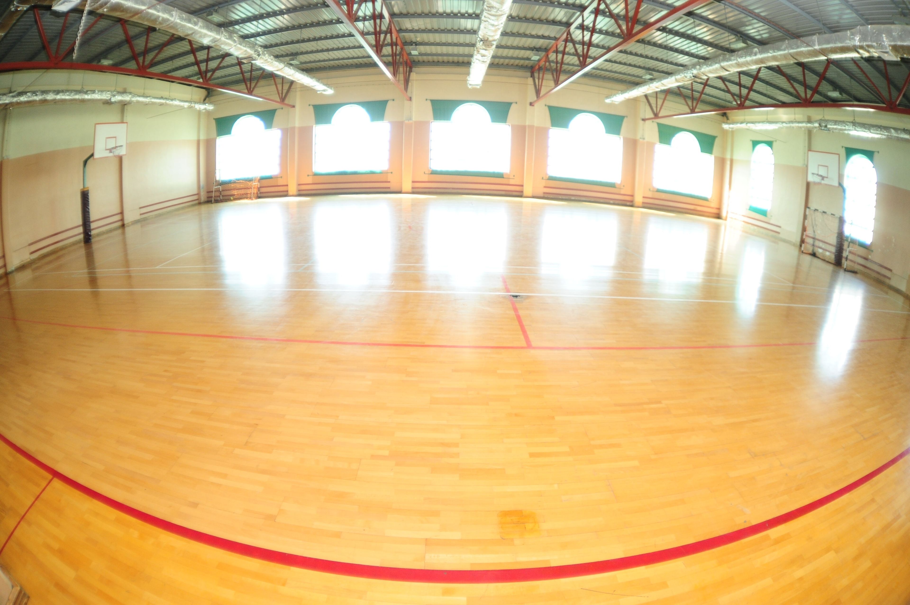 A large indoor gymnasium with a wooden floor and a basketball hoop.
