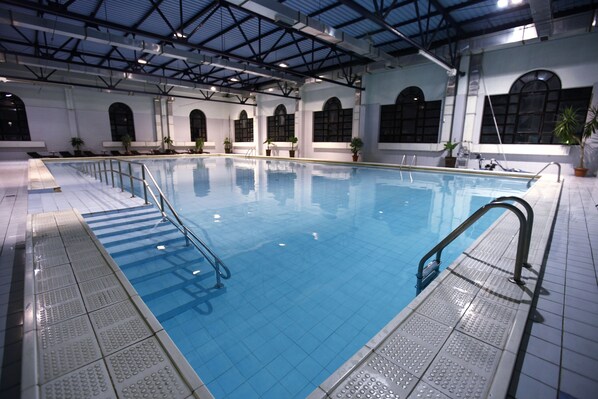 An indoor swimming pool with clear blue water, tiled walls, and a high ceiling with visible beams.