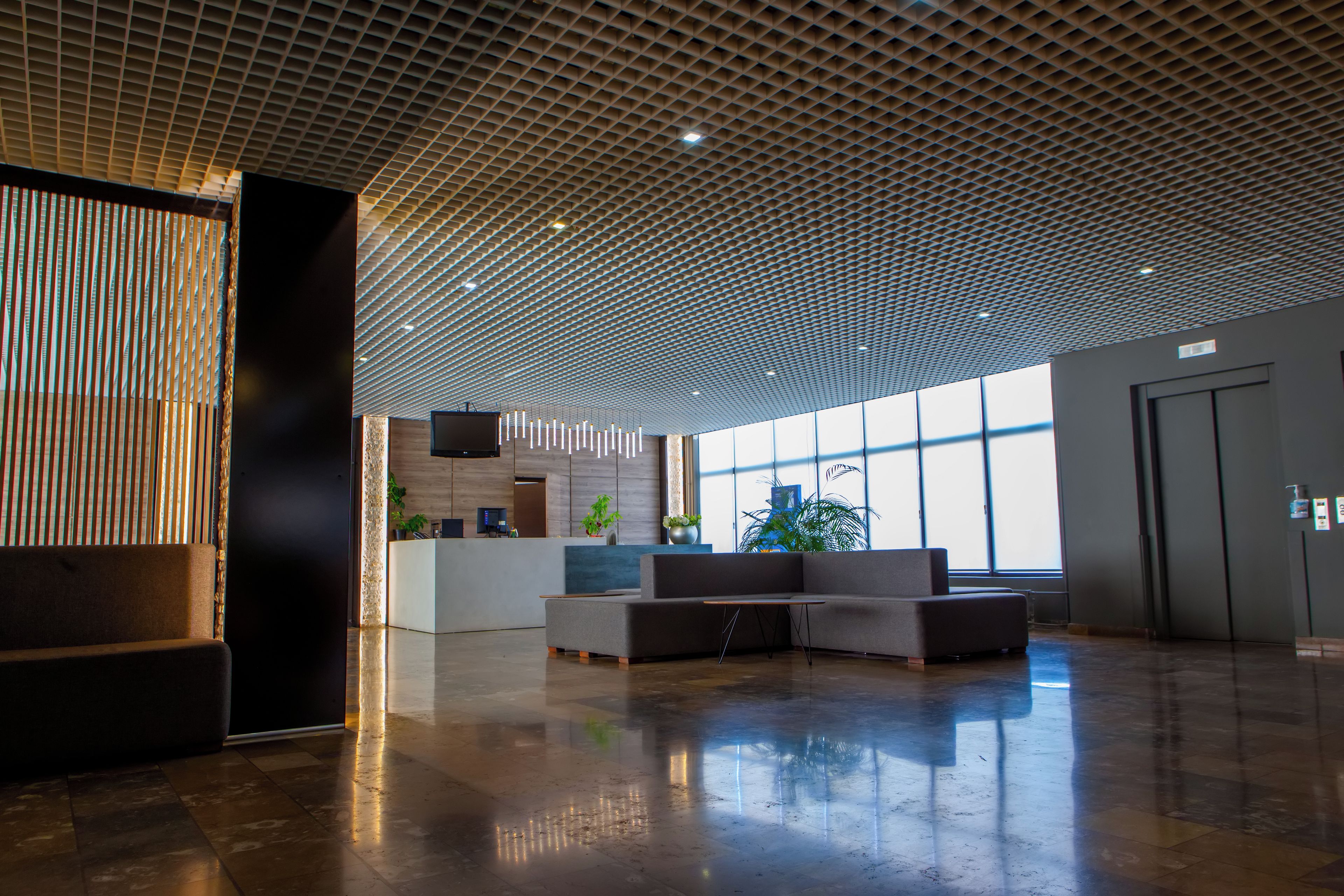 Eine geräumige Lobby mit modernem Deckenstil, einem Empfangsbereich, einer Sitzecke und großen Fenstern, die viel Tageslicht hereinlassen.