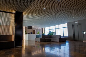 A spacious lobby with a modern ceiling design, a reception desk, seating area, and large windows allowing natural light. - Cross Health Center (Yerevan)