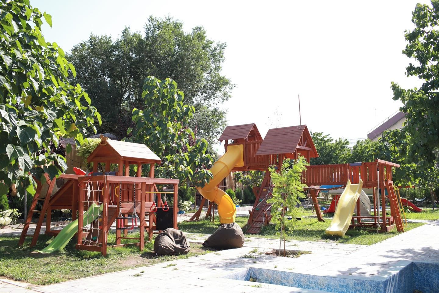 Un parque infantil con estructuras de madera, que incluyen toboganes y zonas de escalada, rodeado de árboles.