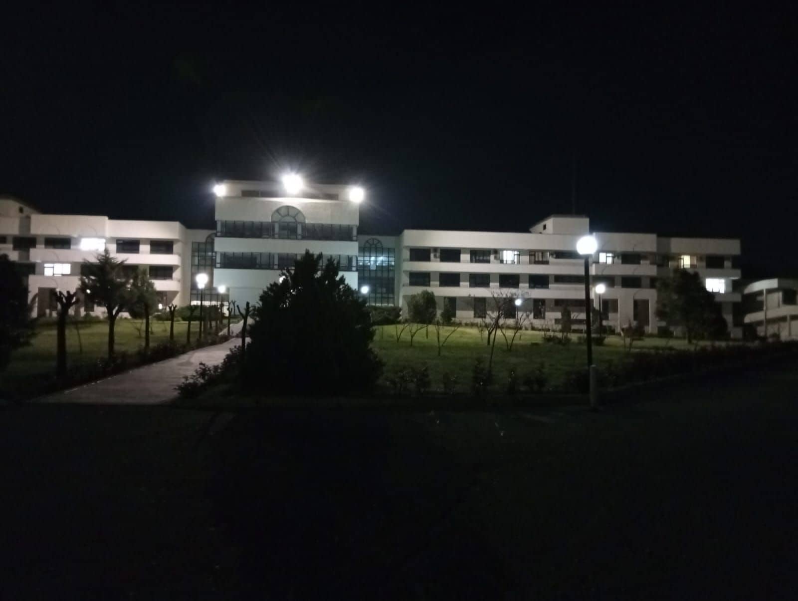 A multi-story building with a central entrance and a well-lit facade at night.