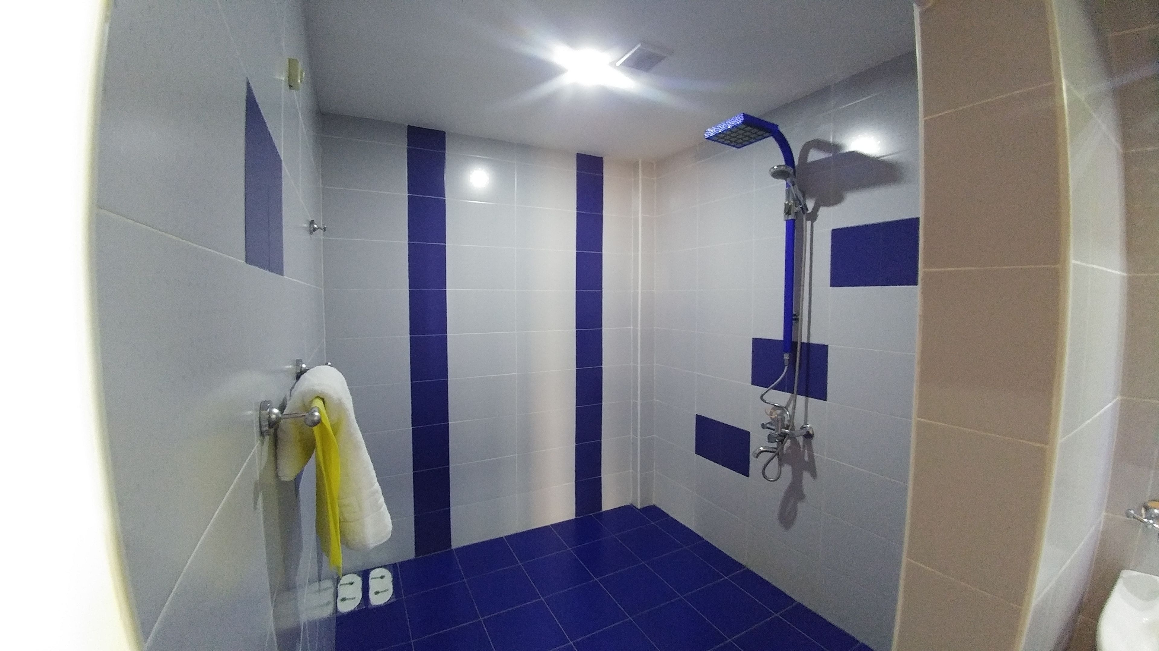 Ein Badezimmer mit blauen und weißen Fliesen, einer Dusche und einem gelben Handtuch an einem Haken.