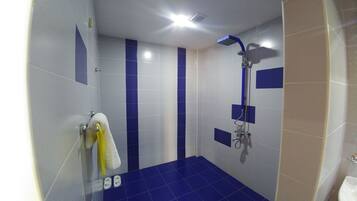Ein Badezimmer mit blauen und weißen Fliesen, einer Dusche und einem gelben Handtuch an einem Haken.