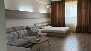 Een moderne hotelkamer met een bank, een bed, een bijzettafeltje en een groot raam met gordijnen.