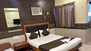 Hotelkamer met een groot bed, nachtkastje, spiegel, airconditioning en een raam met gordijnen.
