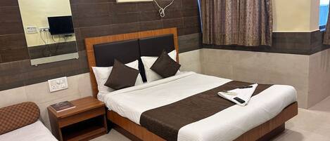 A hotel room with a large bed, a bedside table, a mirror, an air conditioning unit, and a window with curtains.