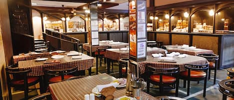 A restaurant interior with multiple tables and chairs, a staircase, and a wall displaying various items.