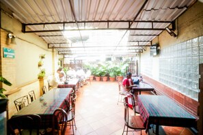 Un comedor interior con mesas y sillas, plantas en macetas y una pared de azulejos.