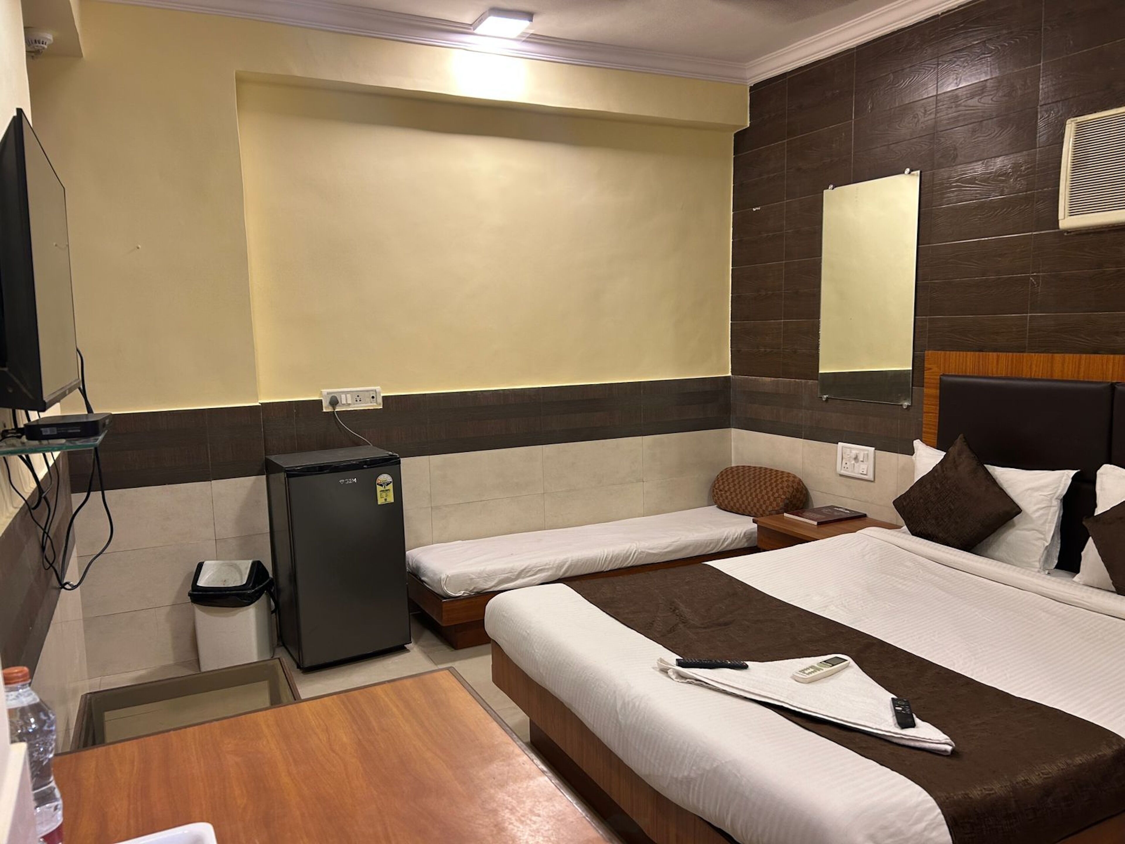A hotel room with a large bed, a smaller bed, a desk, a refrigerator, and a television.