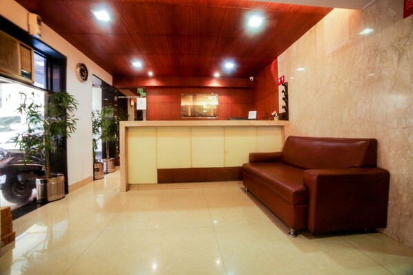Un área de recepción con techo de madera, un sofá de cuero marrón, un mostrador de recepción y plantas en macetas.