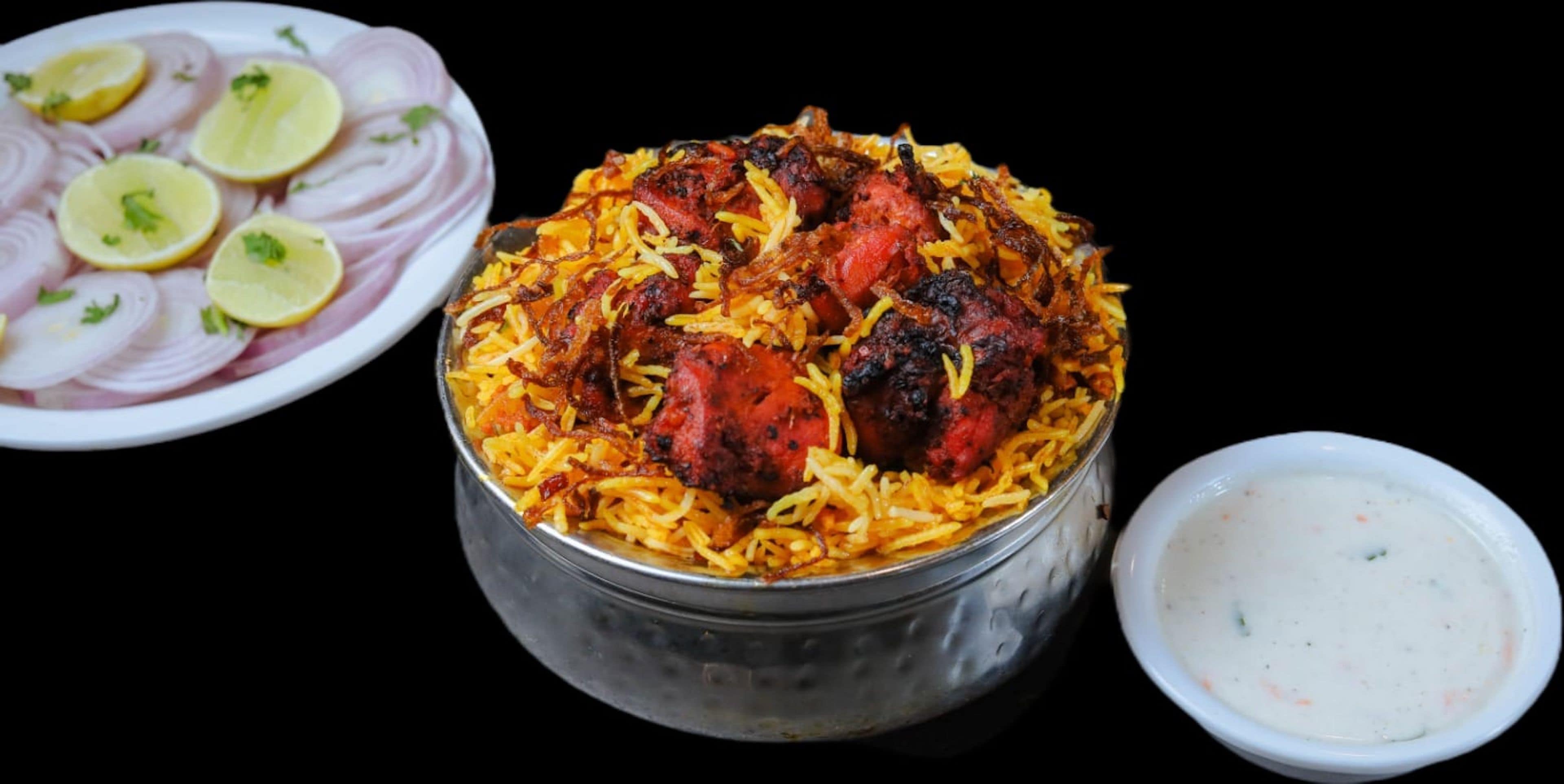A meal consisting of biryani, a bowl of raita, and sliced onions with lemon.