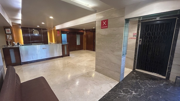 Vestíbulo de hotel con mostrador de recepción, un reloj, un cartel de prohibido fumar y un ascensor.