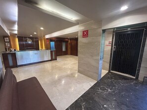 A hotel lobby with a reception desk, a clock, a no smoking sign, and an elevator. - Hotel Lucky Near Nesco (Mumbai)